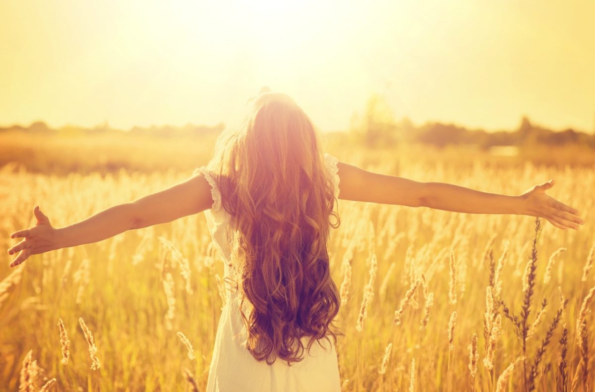 Dark haired girl with open arms looking at the sun