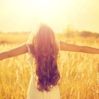 Dark haired girl with open arms looking at the sun