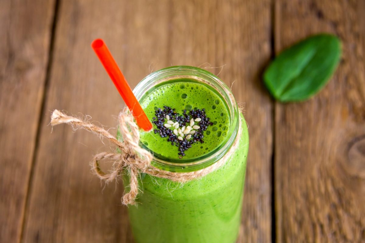 Green smoothie with heart of seeds in jar over rustic wooden background