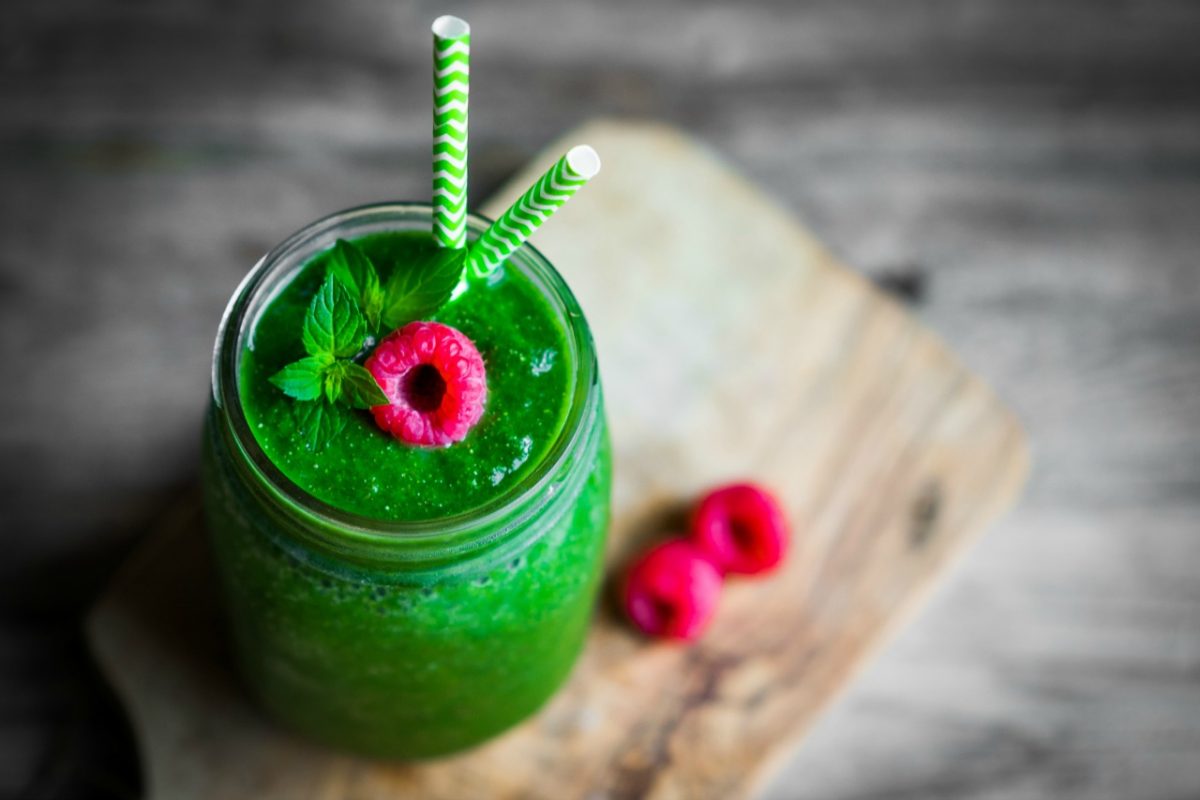 Green smoothie ina mason jar with a raspberry on top on rustic wooden background