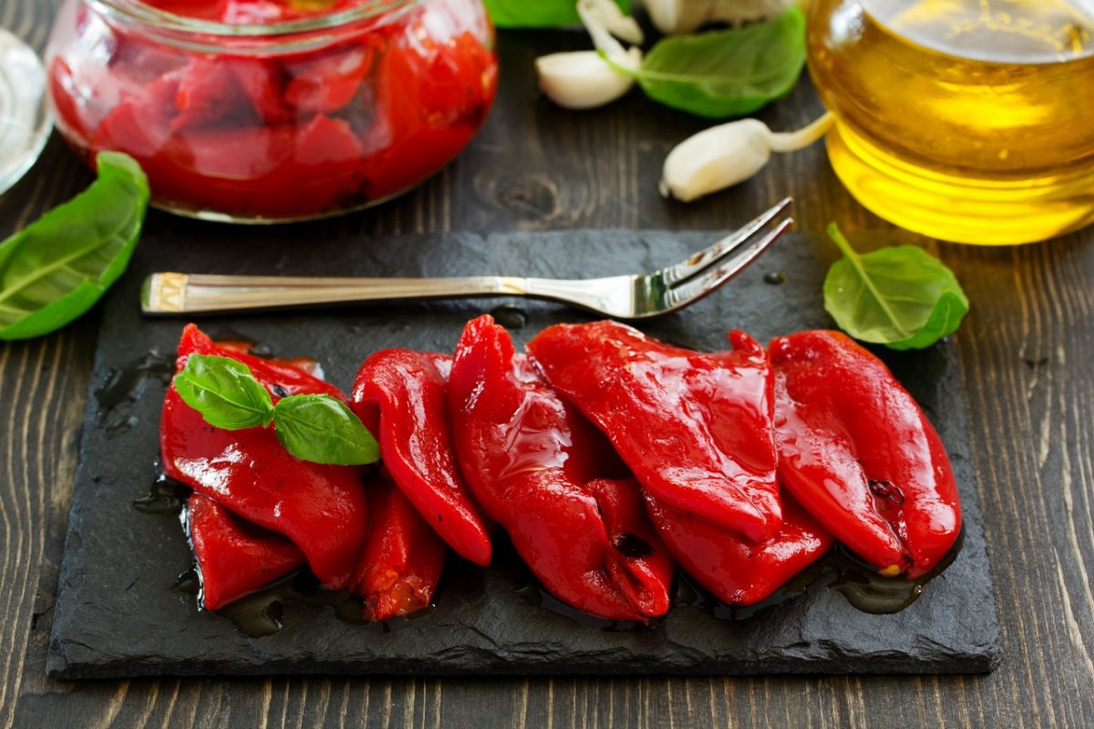 Roasted red peppers on a dark background with garlic and olive oil on the side