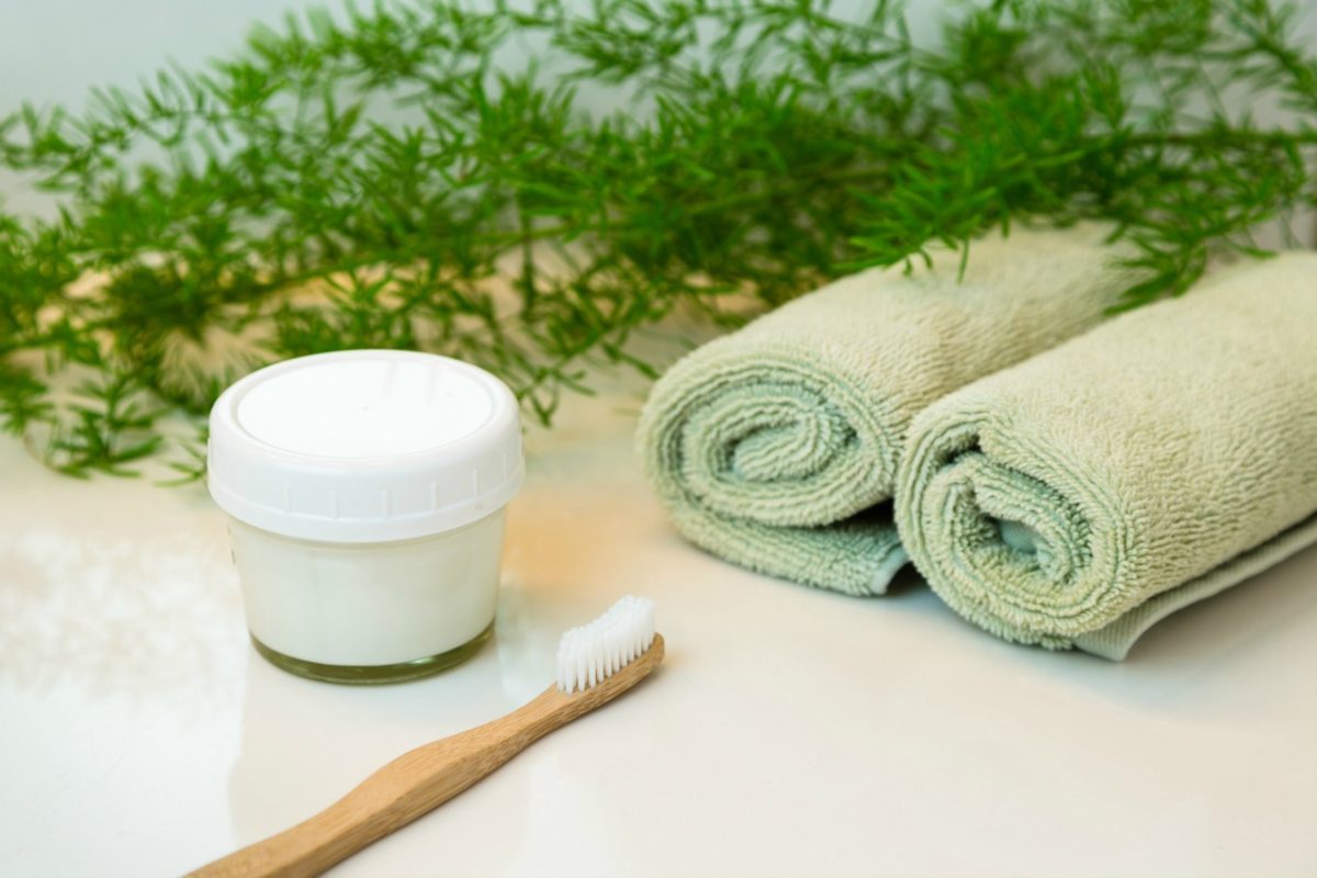 Homemade toothpaste in mason jar and bamboo toothbrush. Rolled green towels in a spa setting.